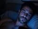 Gay man lying in bed at night scrolling phone seeking validation in Chicago